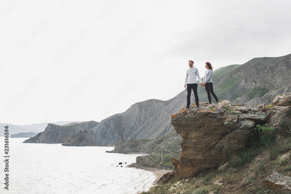 Young couple walking on nordic sea coast with mountain view in spring, casual style clothing sweaters and jeans Young couple walking on nordic sea coast with mountain view in spring, casual style clothing sweaters and jeans