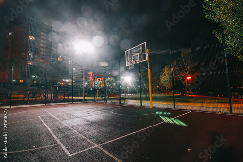 Illuminated basketball playground with red pavement, modern new basketball net and lens flares on background. 