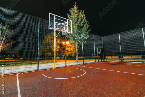 Illuminated basketball playground with red pavement, modern new basketball net and lens flares on background. 