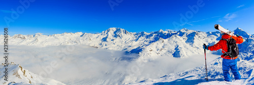 Ski in winter season, mountains and ski touring man on the top in sunny day in France, Alps above the clouds.