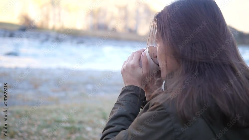 Happy woman with a drink admires the view around. Mountains, river, hot tea