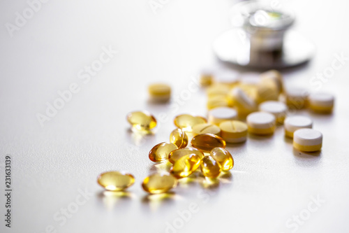 The medicines and fish oil tablets on the white surface with stethocope in the natural light