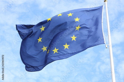 Closeup of single european flag with twelve yellow stars waving in the wind in front of blue sky