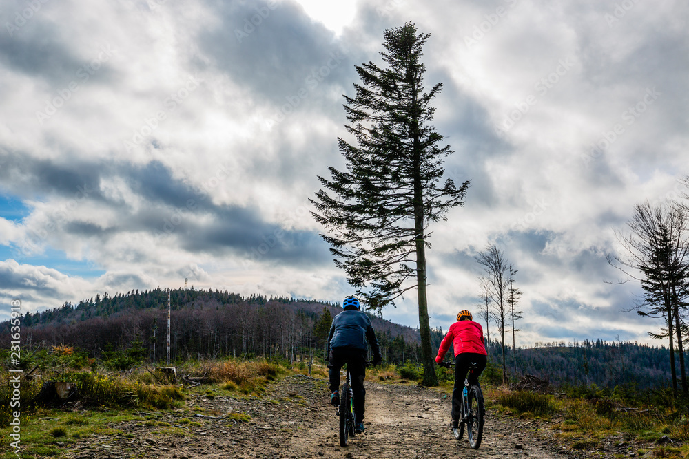 Cycling woman and man at Beskidy mountains autumn forest landscape. Couple riding MTB enduro track. Outdoor sport activity.