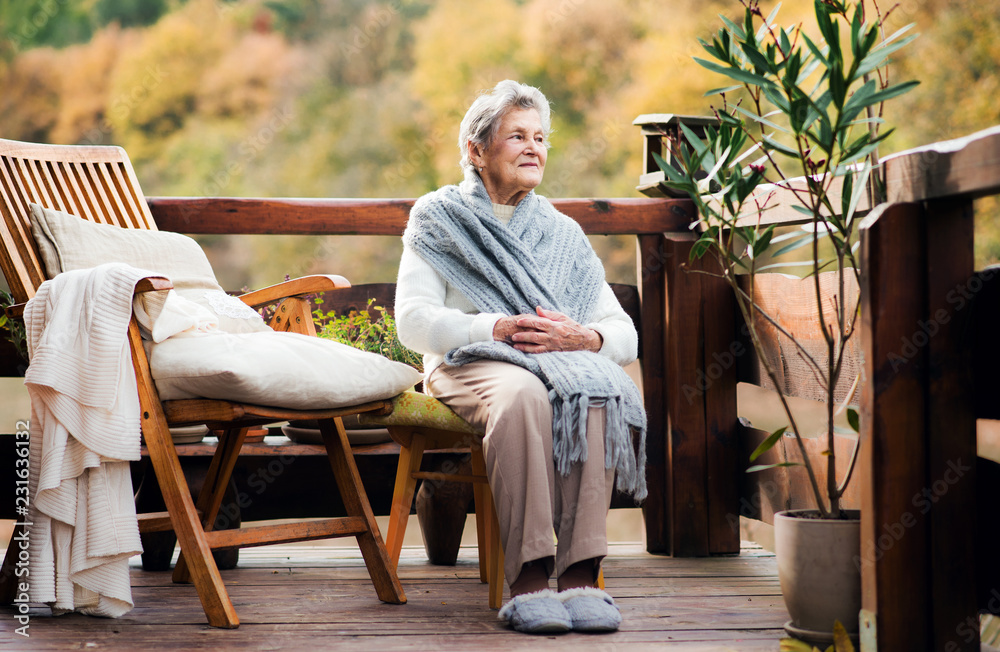 Fototapeta premium An elderly woman sitting outdoors on a terrace on a sunny day in autumn.
