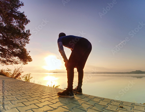 Short break for breath. Silhouette of active man on lake beach