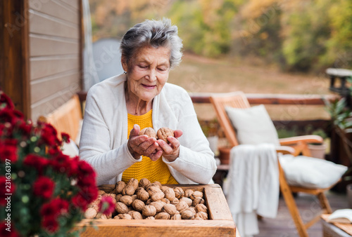 An elderly woman outdoors on a terrace on a sunny day in autumn, holding walnuts.