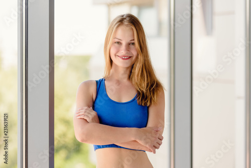 Portrait of beautiful fit smiling sportswoman posing in front of window