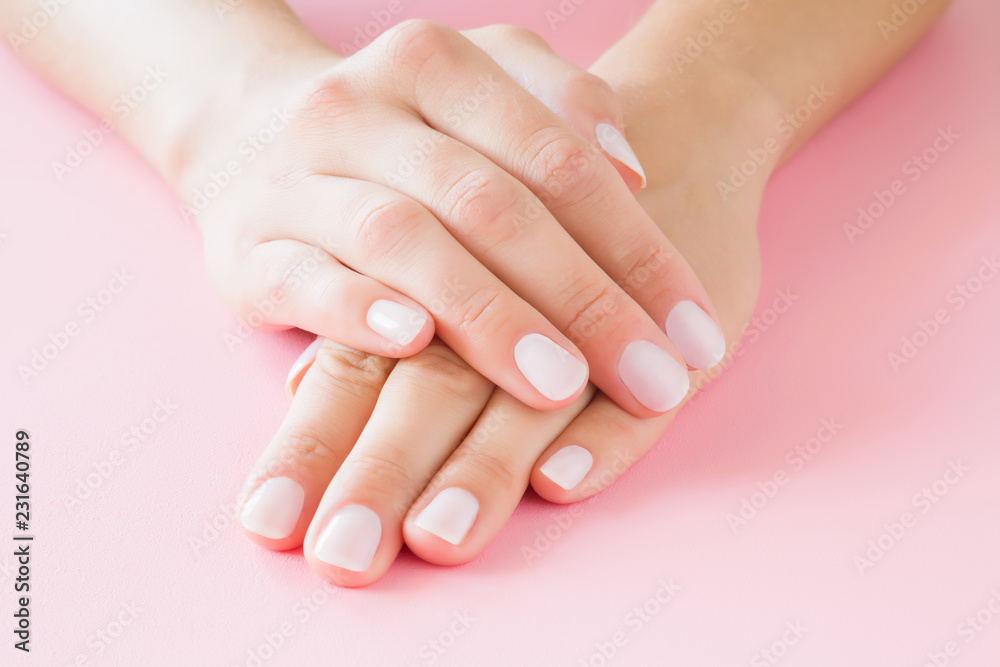 Young, perfect woman's hands with light nails on pastel pink table. Care about clean, soft and smooth skin. Manicure, pedicure beauty salon.