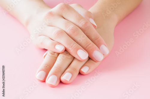 Young  perfect woman s hands with light nails on pastel pink table. Care about clean  soft and smooth skin. Manicure  pedicure beauty salon.