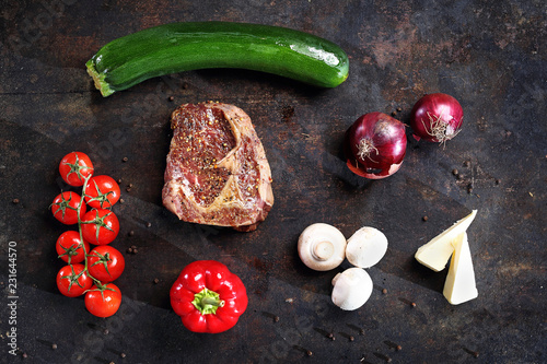 Stek z karkówki. Mięso i warzywa, składniki potrawy ułożone w kompozycji na ciemnym tle.