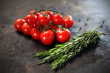 Pomidory i rozmaryn Gałązka pomidorów koktajlowych i aromatycznych ziół rozmarynu na czarnym tle.