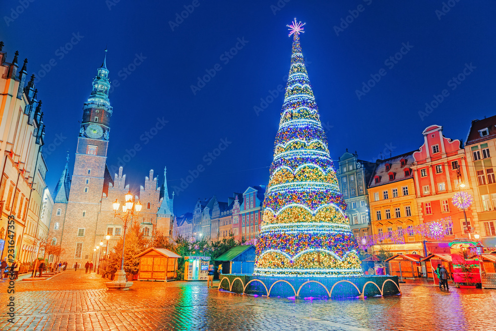 Illuminated Christmas tree at central Square of old city on Christmas Market in Wroclaw, Poland. New Year ambiance, illuminated and ornamented festive city. Night scene. European traditions. - obrazy, fototapety, plakaty 