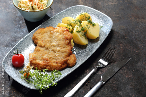 Kotlet schabowy z ziemniakami. Kotlet smażony w panierce, ziemniaki z wody, surówka z białej kapusty.