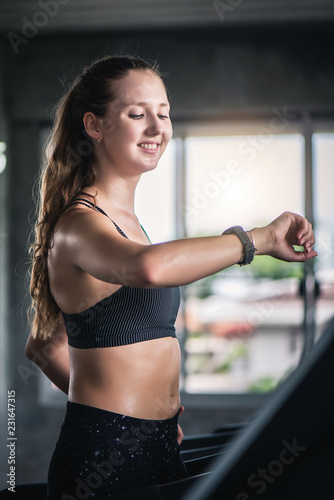 Attractive pretty Caucasian woman running on treadmill and check heart rate with smart watch at gym. 