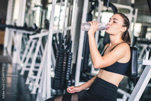 Attractive young Caucasian beautiful woman get resting and drink some water from plastic bottle after workout at gym 
