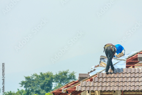 Construction roofer installing roof tiles at house building site