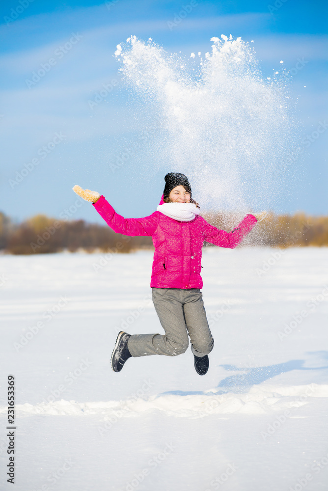 Happy winter fun young girl playing throwing snow with arms up open in freedom enjoying the cold season