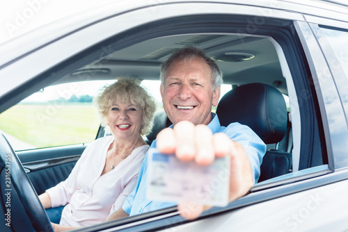 Portrait of a happy senior man showing his available driving license while sitting in the car next to his cheerful wife photo