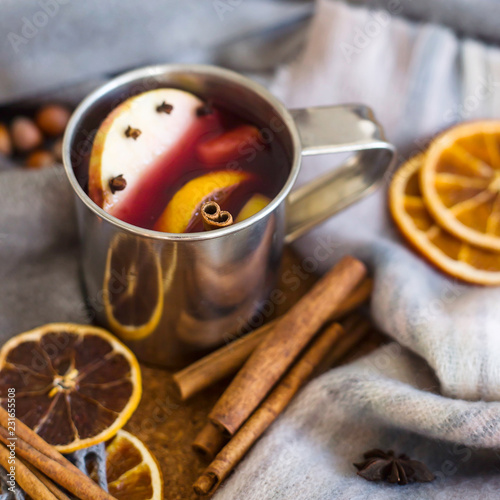 Mulled wine with apple, orange, clove, cinnamon and anise in a metal mug among winter plaids, scarves and sweaters. Hot drink on the eve Christmas eve