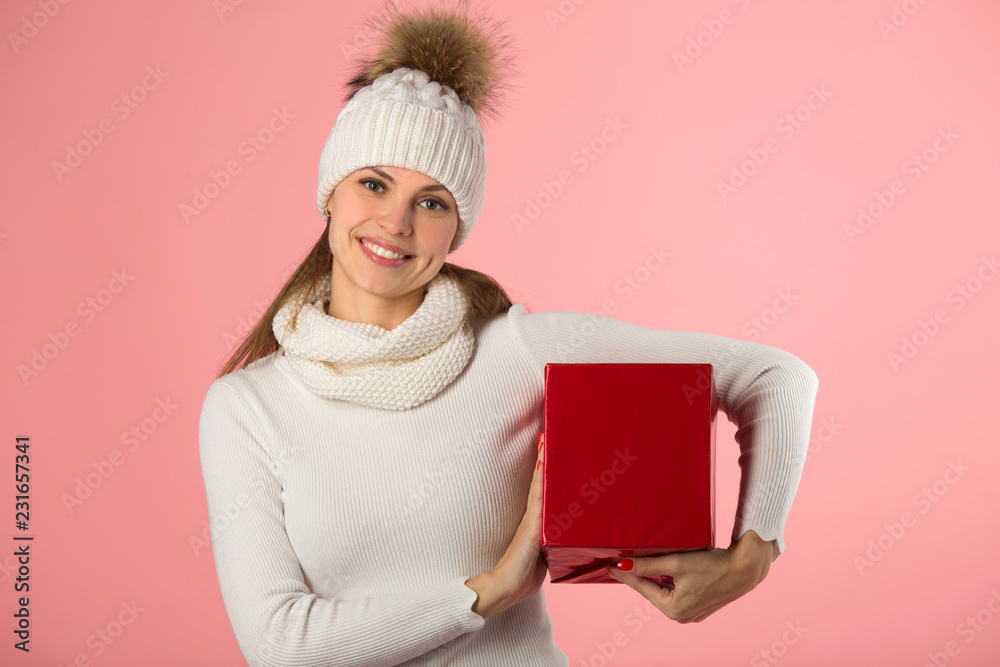 beautiful young girl in winter hat with a gift in hand on a pink background