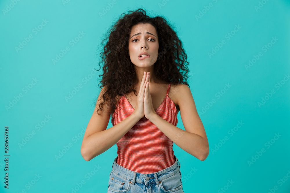 Image of curly woman 20s wearing casual holding palms together, standing isolated over blue background Image of curly woman 20s wearing casual holding palms together, standing isolated over blue background