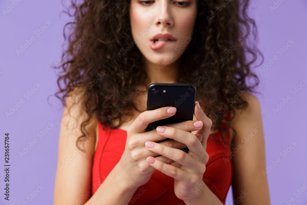 Image of cute woman 20s wearing red dress holding black smartphone, standing isolated over violet background Image of cute woman 20s wearing red dress holding black smartphone, standing isolated over violet background