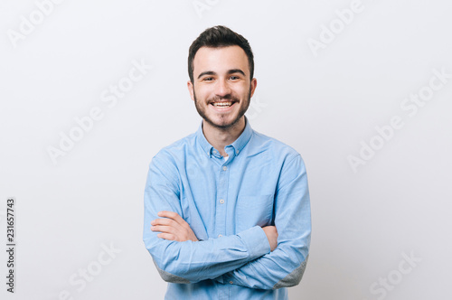 Portrait of cheerful young man in casual with crossed arms smiling over white background and looking at the camera
