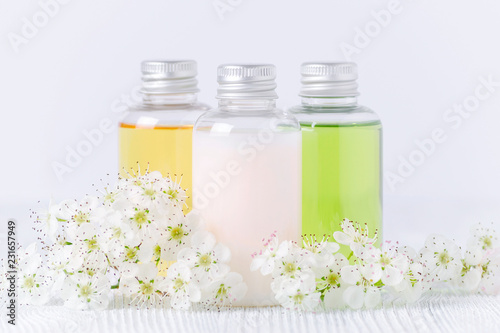 natural cosmetic bottles with fresh flowers on gray background