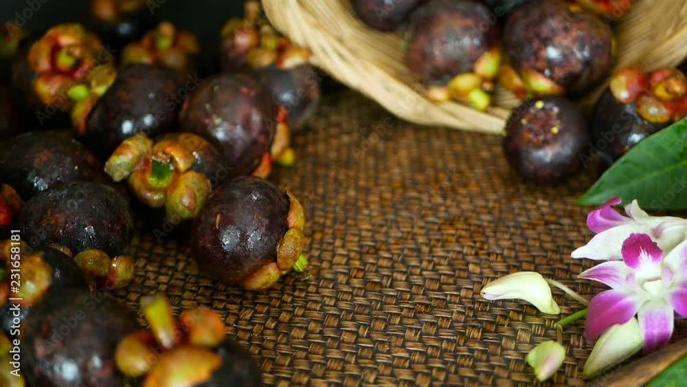 Top view of fresh delicious harvested mangosteens on wooden table. Thai organic purple fruit in the basket. Exotic natural blurred background with tropical flower. Healthy food and eating concept. Top view of fresh delicious harvested mangosteens on wooden table. Thai organic purple fruit in the basket. Exotic natural blurred background with tropical flower. Healthy food and eating concept.