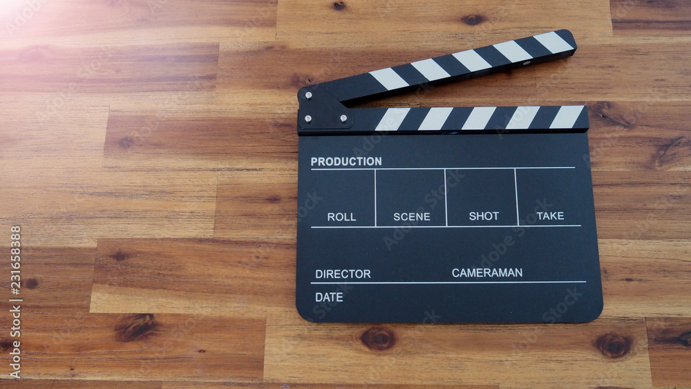 Clapper board or clap board or movie slate use in video production , film, cinema industry. It's black color on wood background with flare light.