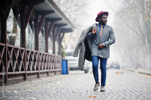 Stylish African American man model in gray coat, jacket tie and red hat posed at foggy weather street. photo