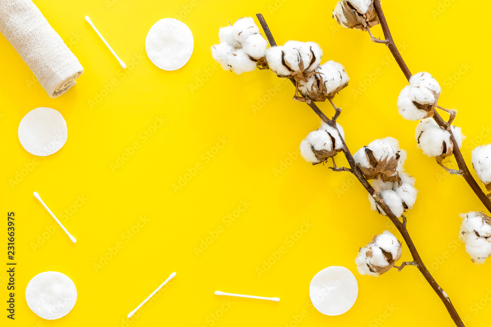 Fototapeta premium Products made of cotton. Bath accessories. Towels, cotton pads and swabs near dry cotton flowers on yellow background top view copy space frame