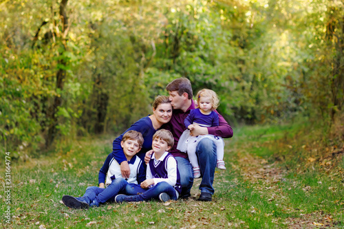 Portrait of young parents with three children. Mother, father, two kids brothers boys and little cute toddler sister girl having fun together in autumn forest. Happy family of five