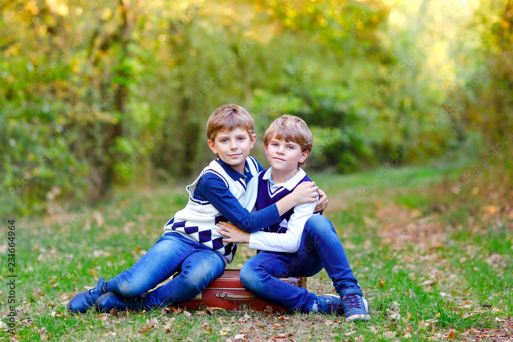 Portrait of little school kids boys sitting in forest. Happy children, best friends and siblings having fun on warm sunny day early autumn. Twins and family, nature and active leisure. Portrait of little school kids boys sitting in forest. Happy children, best friends and siblings having fun on warm sunny day early autumn. Twins and family, nature and active leisure.