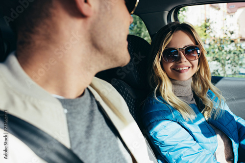 smiling woman in sunglasses looking at boyfriend in car