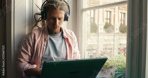 Cheerful and hard-working man listening to music as using the laptop, working in quiet home atmosphere to achieve better result