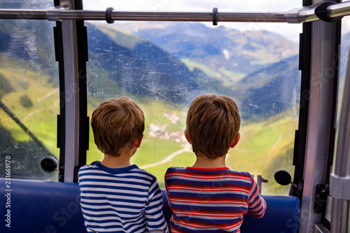 Two little boys sitting inside of cabin of cable car and looking on mountains landscape.
