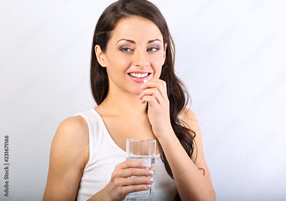 Happy smiling positive woman eating the pill and holding the glass of water in the hand on white background. Closeup portrait Happy smiling positive woman eating the pill and holding the glass of water in the hand on white background. Closeup portrait