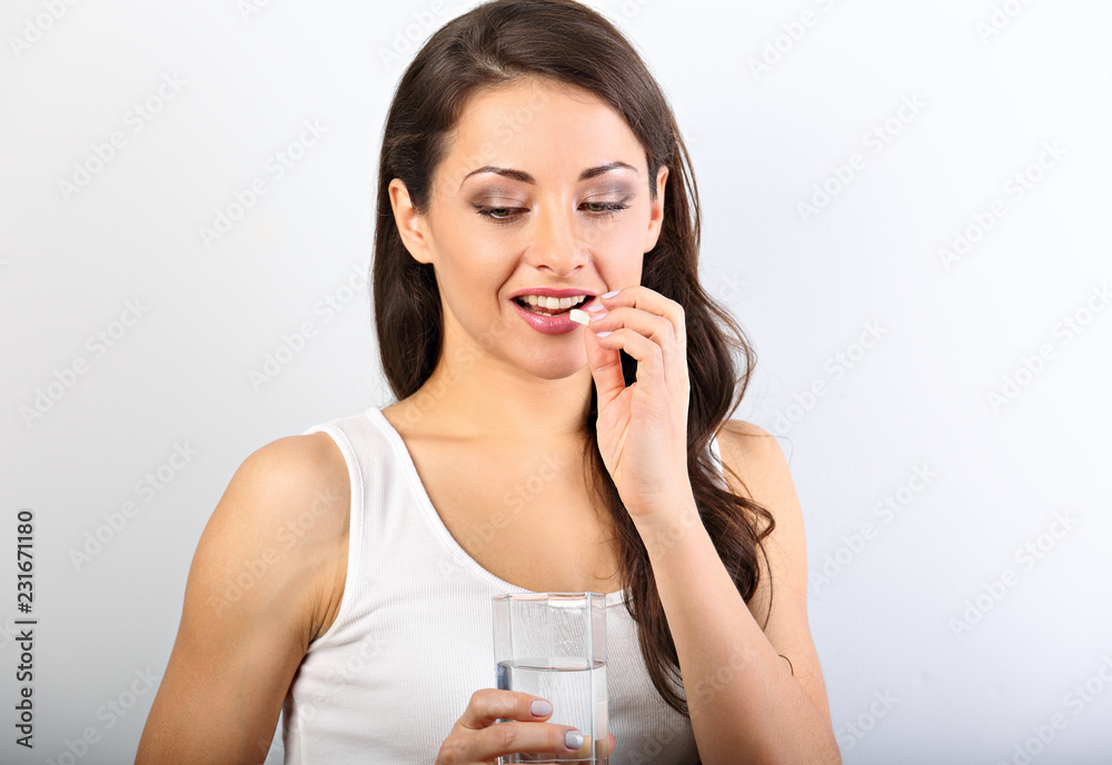 Happy smiling positive woman eating the pill and holding the glass of water in the hand on white background. Closeup portrait Happy smiling positive woman eating the pill and holding the glass of water in the hand on white background. Closeup portrait
