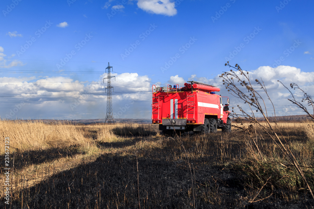 Obraz premium Red firetruck car Ural rides through the autumn field with yellow and faded grass against the blue sky and clouds. The concept of extinguishing forest fires in USA