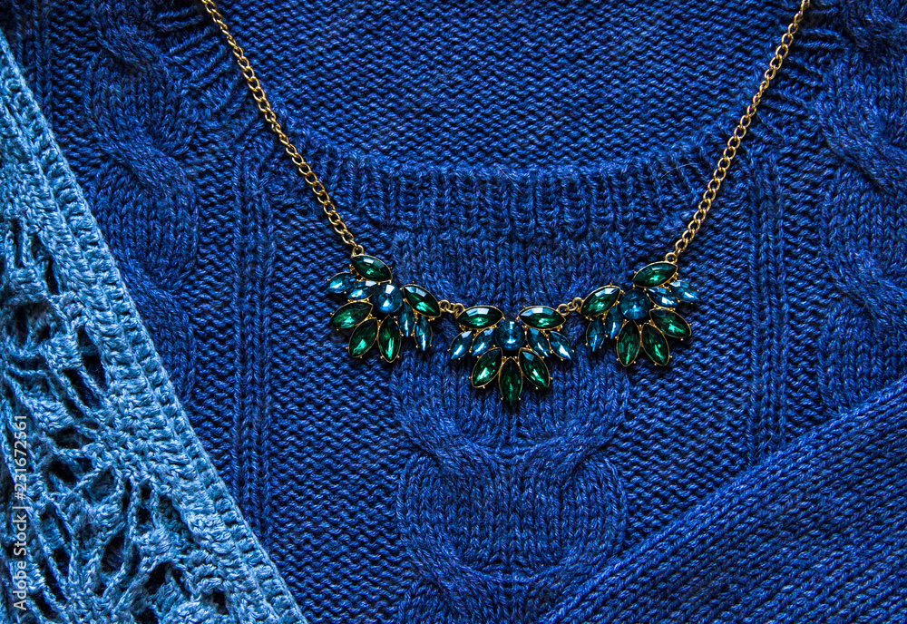 Knitting and hand made concept-blue knitted sweater and green necklace with gold chain close-up. Knitting texture. Part of knitted clothing. Autumn, winter concept. Top view, copy space, flat lay.