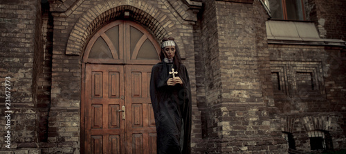 Young nun is standing and praying with cross in her hands on temple door background. © Stanislav