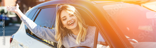 portrait of happy blond woman waving to someone while driving car