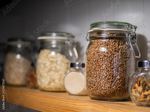 Various uncooked cereals, grains, beans and pasta for healthy cooking in glass jars on wooden table, white background, close-up. Clean eating, vegan, balanced dieting food concept