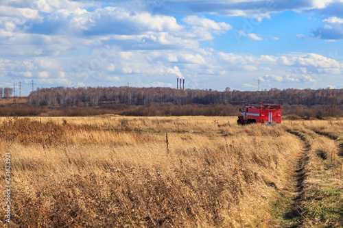 Red firetruck car Ural rides through the autumn field with yellow and faded grass against the blue sky and clouds. The concept of extinguishing forest fires in USA
