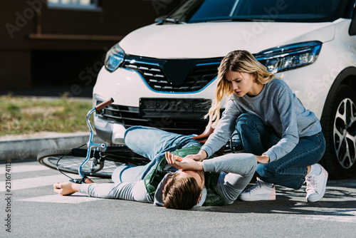 young woman trying to help injured cyclist at car accident