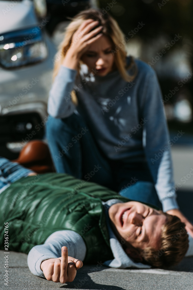Fototapeta premium injured young man lying on road and showing middle finger after traffic collision