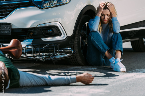cropped shot of cyclist lying on road and scared woman crying after traffic collision