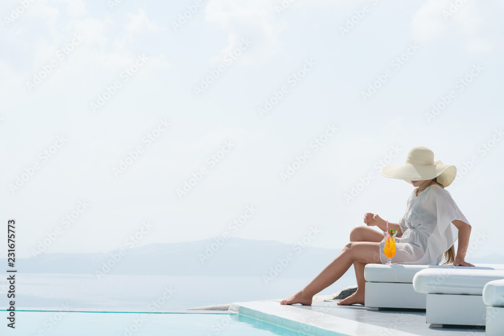 young woman drinking a cocktail enjoying a magnificent view of Santorini near the pool